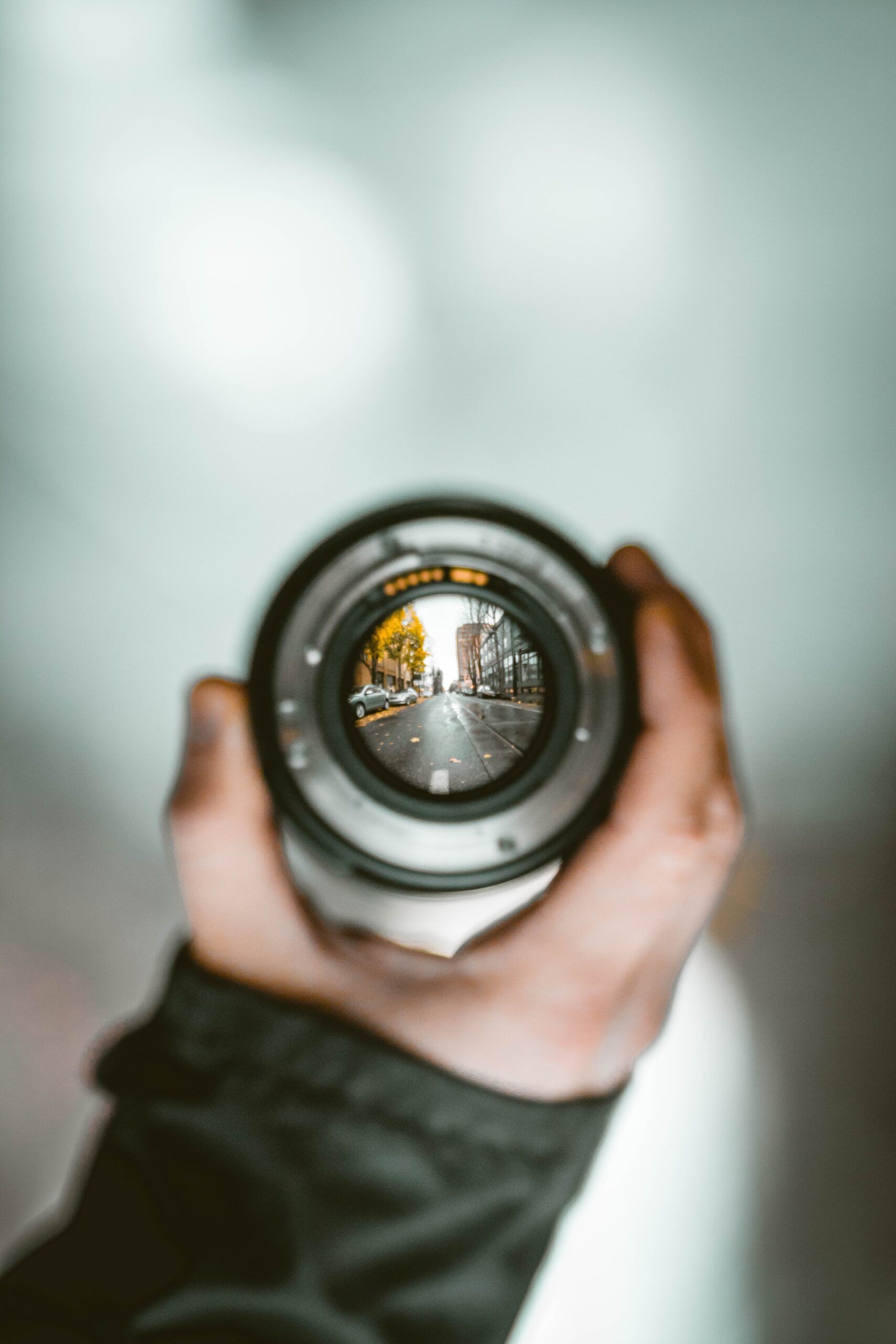 Man holding up a camera lense with a blurred background but clarity showing through the lense