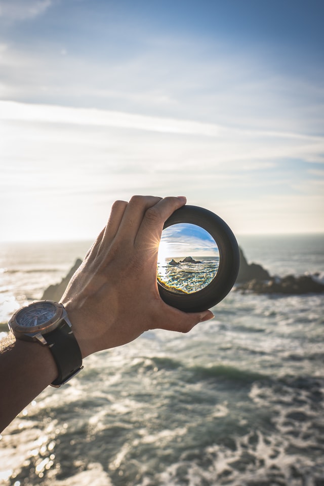 Man holding lense and looking at the rocks out at sea